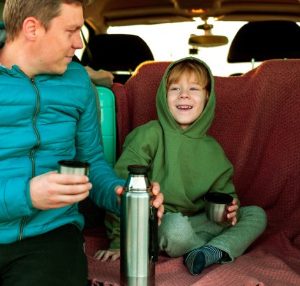 Dad and his kid drink tea while spending the comfortable journey