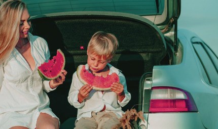 A kid and her mom eat watermelon while on a comfortable journey