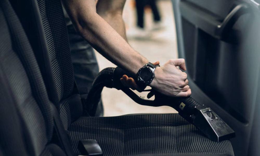 A man is vacuuming the rear car interior