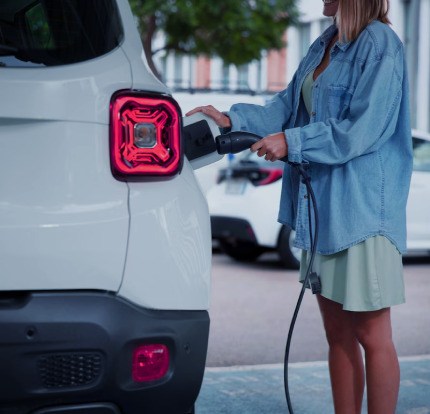 White used electric vehicle is charged by a women