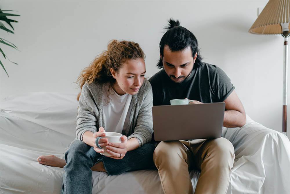 A couple on the couch look up into the laptop for selling their motorcycle