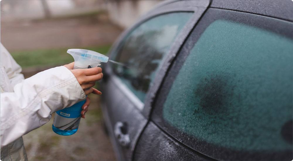 A woman uses spray to defrost car windows